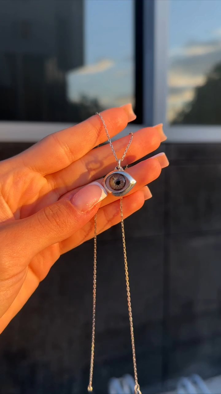 Silver almond eye pendant with a hand-painted iris, held up at sunset